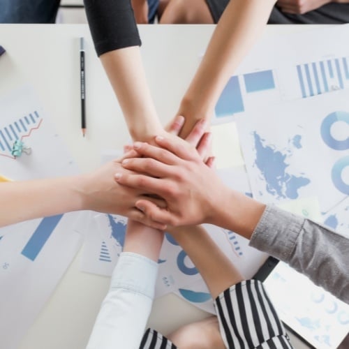 people gathered around a table with charts and diagrams with their hands in the middle