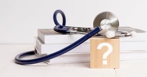 stack of books with a stethoscope and a block with a question mark on it