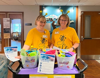Wearing bee-themed outfits, Wendy Hildenbrandt (left) and Linnie Clark show off the prizes and educational materials for the “Bee Safe for Summer” vaccine clinic event at Morningstar Living in Nazareth, Pennsylvania.