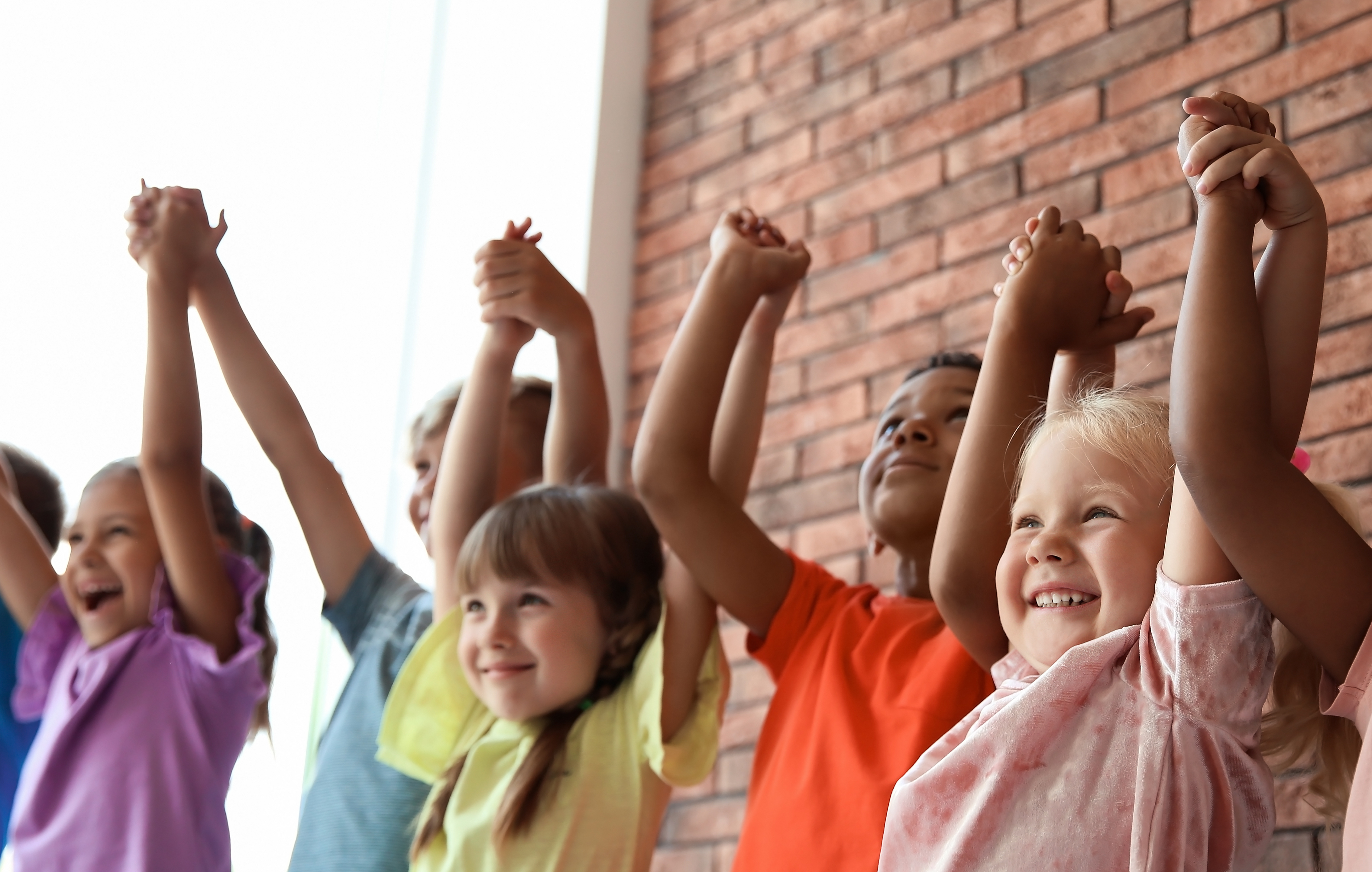 Children holding hands with arms above their heads smiling and happy
