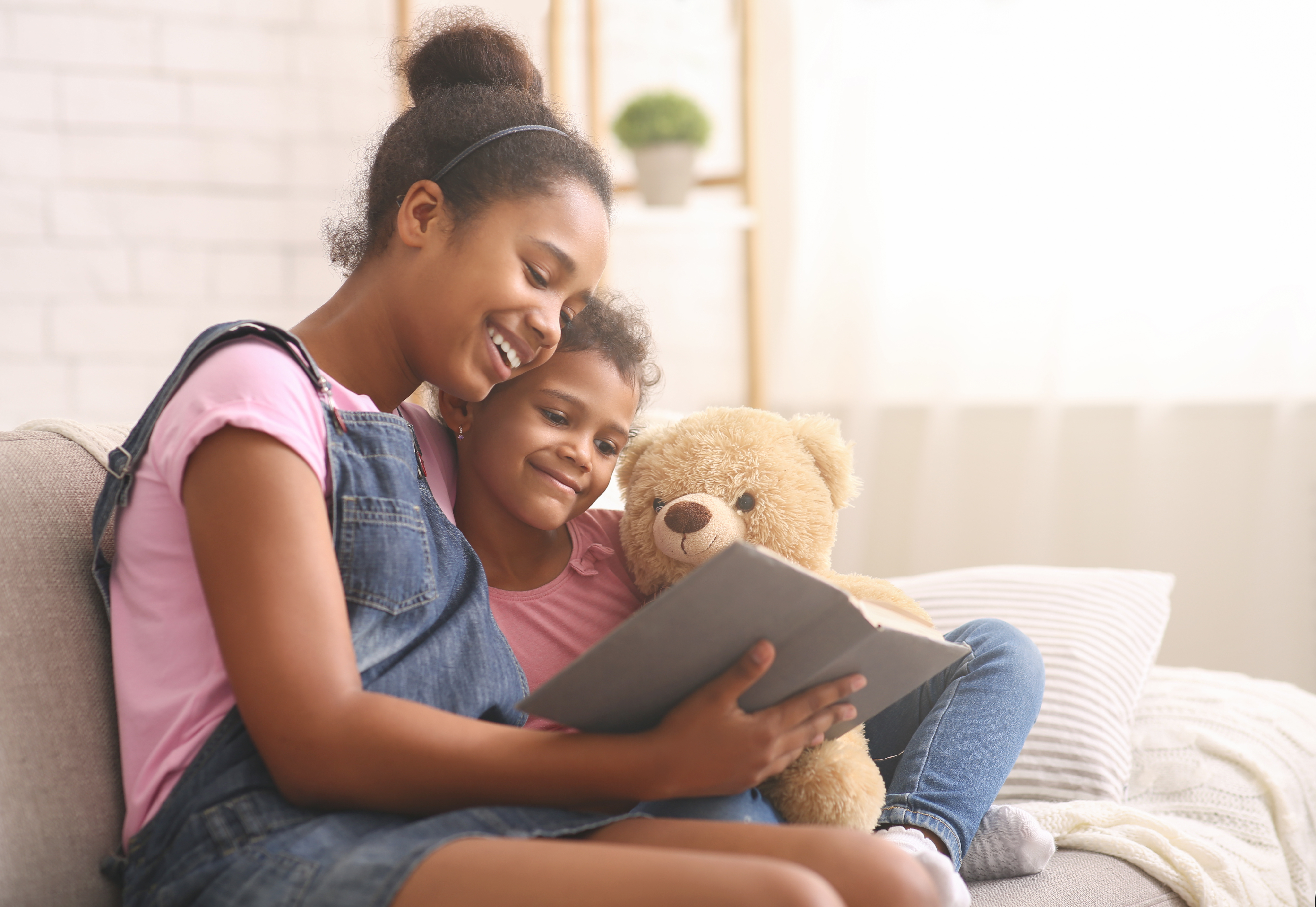 sister reading book with teddy bear