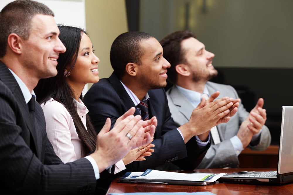 Multi ethnic business group greets somebody with clapping and smiling. Focus on woman